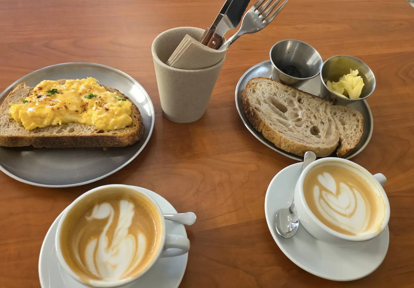 Desayuno con tostada de huevos revueltos, pan de masa madre y dos cafés