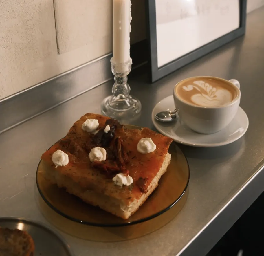 Focaccia con burrata y tomate seco junto a un flat white