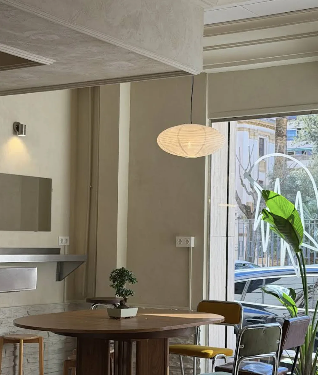 Interior de Gluttoni Cafe con ventanal a la calle, lámpara de papel y bonsái