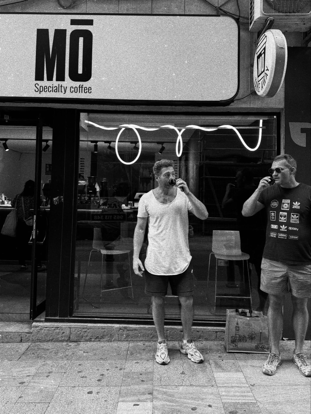 Fachada de MŌ Specialty Coffee en Alicante, dos clientes tomando espresso en la puerta